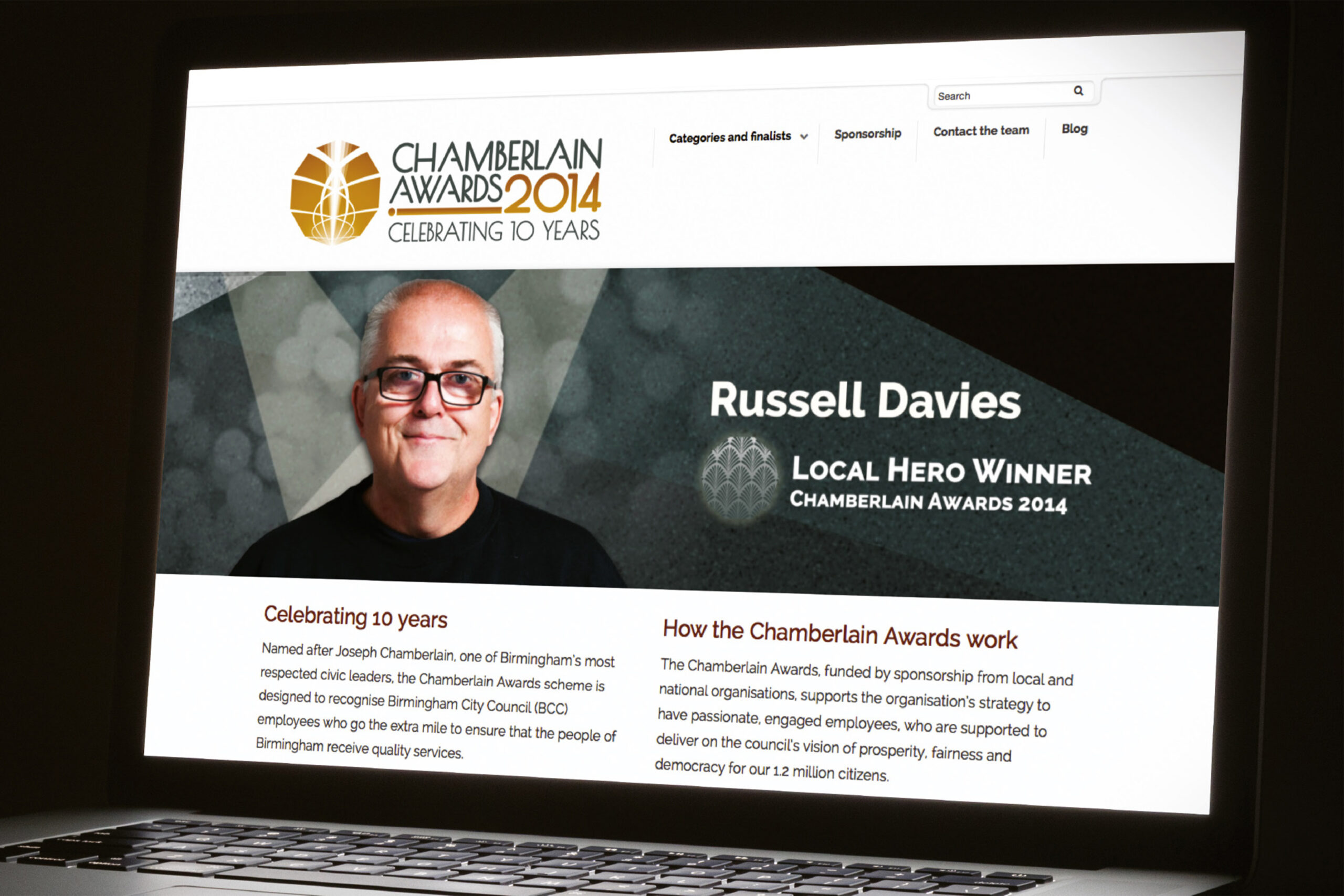 The Chamberlain Awards 2014 website displayed on a laptop in a darkened room. The website displays an image of 'Local Hero' award winner Russell Davies, above text explaining the history of the Chamberlain Awards scheme